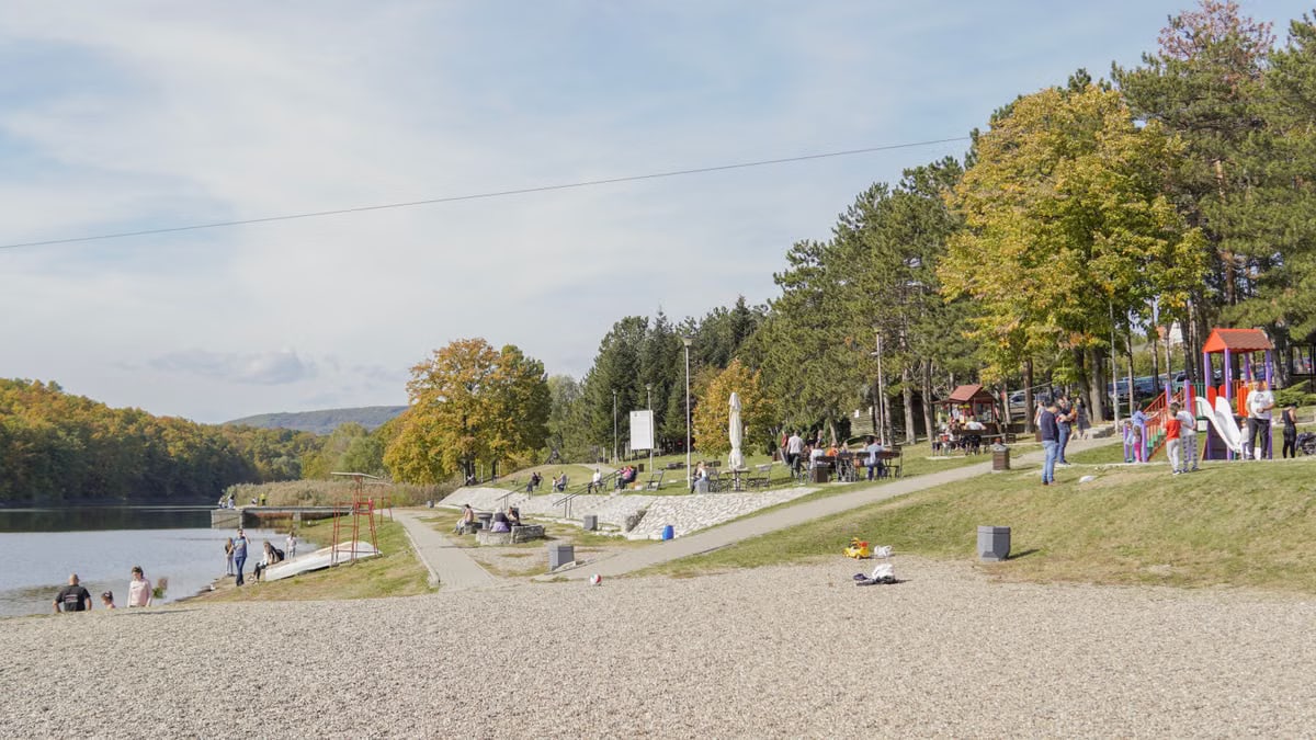 A peaceful park scene with riverside path, trees, and playground, perfect for a family outing.