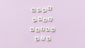Scrabble tiles spell 'Work Hard Dream Big' on a pastel purple surface, top view.